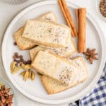 A plate of rectangular glazed shortbread cookies topped with chai tea, garnished with whole cardamom pods, allspice, star anise, and cinnamon sticks.