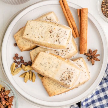A plate of rectangular glazed shortbread cookies topped with chai tea, garnished with whole cardamom pods, allspice, star anise, and cinnamon sticks.
