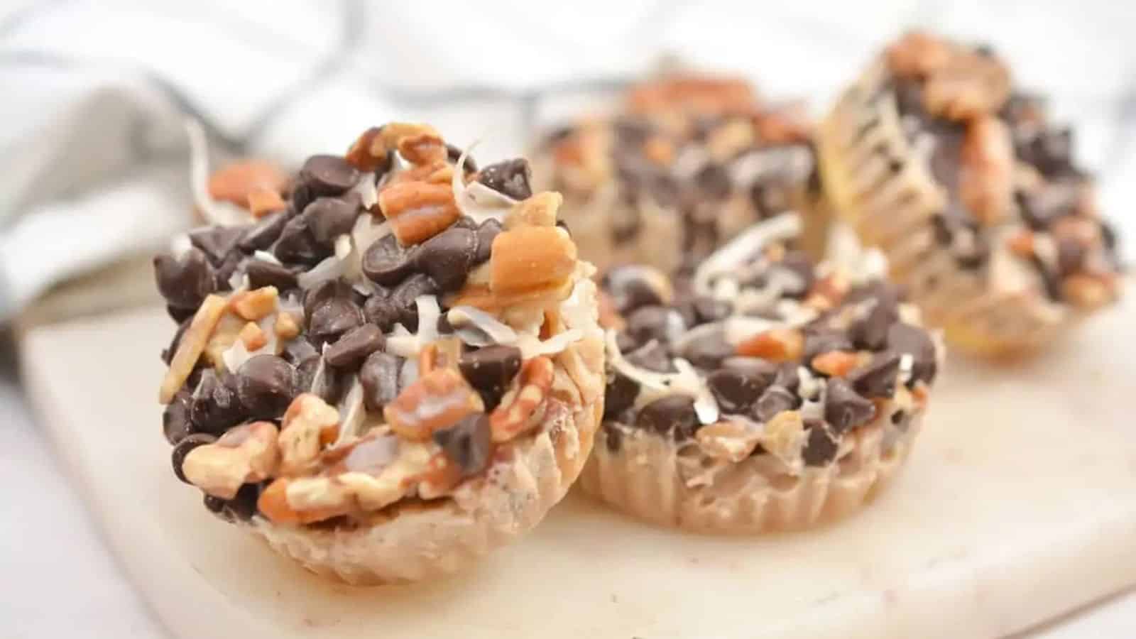 Four nut and chocolate chip dessert cups on a white surface, topped with chopped nuts and chocolate chips.