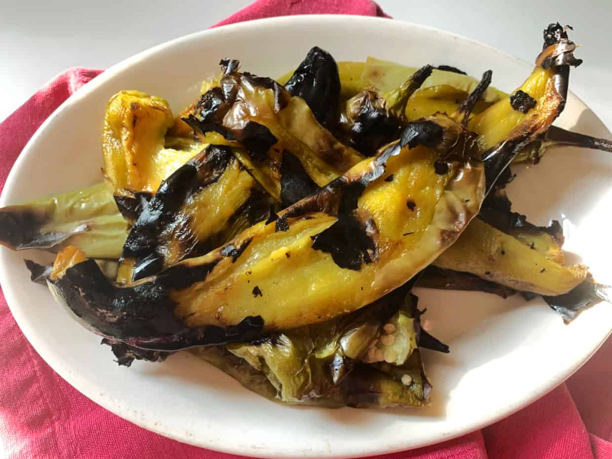 A white plate holds several pieces of charred, roasted Hatch chiles on a red napkin.