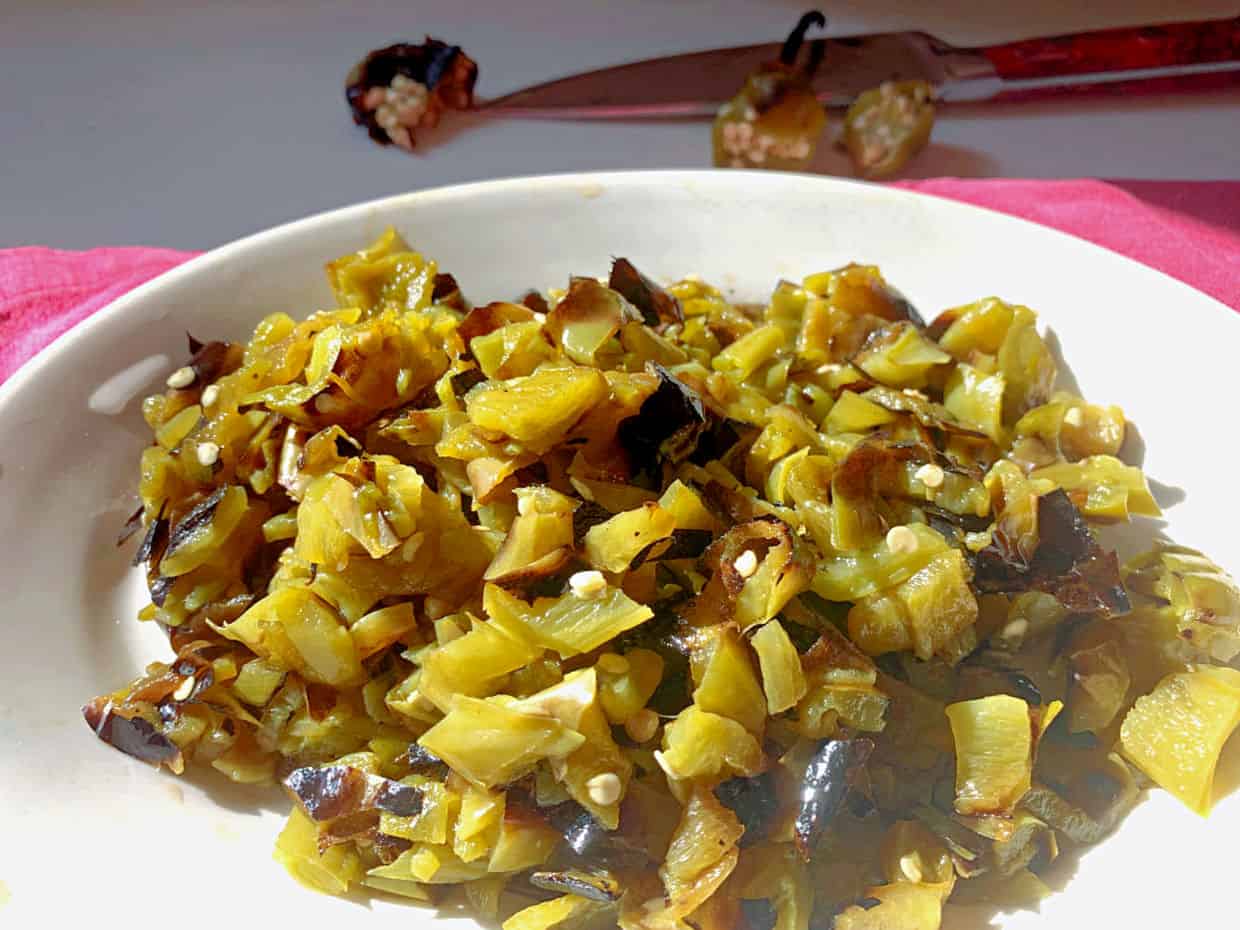 A white plate of chopped roasted Hatch green chiles, with a knife and chile stems visible in the background on a white surface.