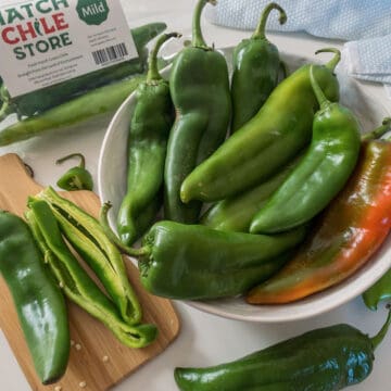 A bowl of fresh green Hatch chile peppers sits next to a cutting board with sliced chiles and a labeled bag reading "Hatch Chile Store Mild.