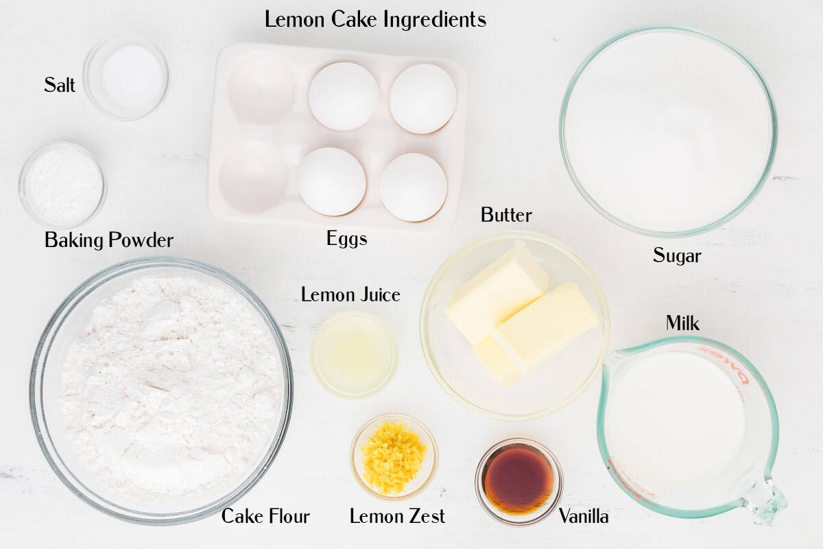 Top-down view of labeled lemon cake ingredients: salt, baking powder, eggs, sugar, butter, milk, lemon juice, lemon zest, cake flour, and vanilla, arranged on a white surface.