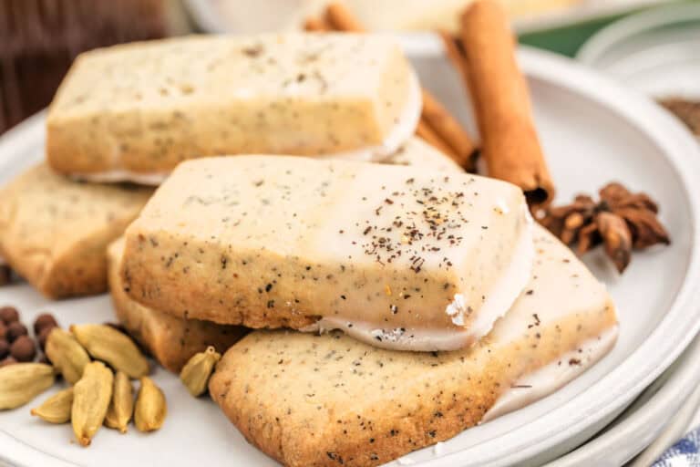 A plate of rectangular iced cookies with Chai tea sprinkles, surrounded by whole spices including cardamom pods and cinnamon sticks.