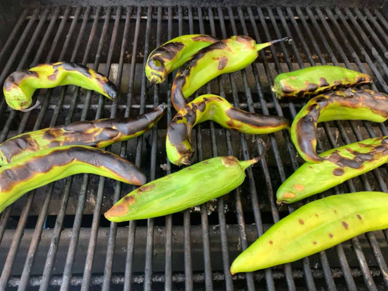 Several long green chiles roasting on a grill, with charred and blistered skins visible on some of the peppers.