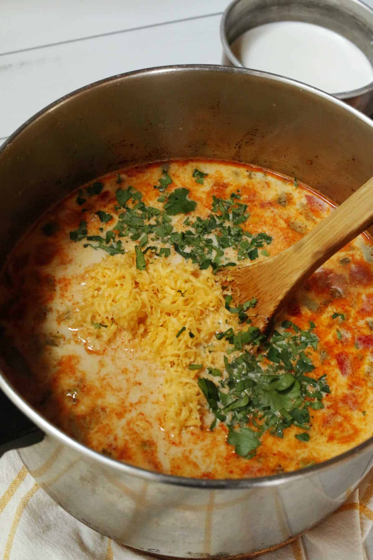 Stirring in cheese and cilantro for a Mexican Corn and Bean Soup that's in a large souppot.