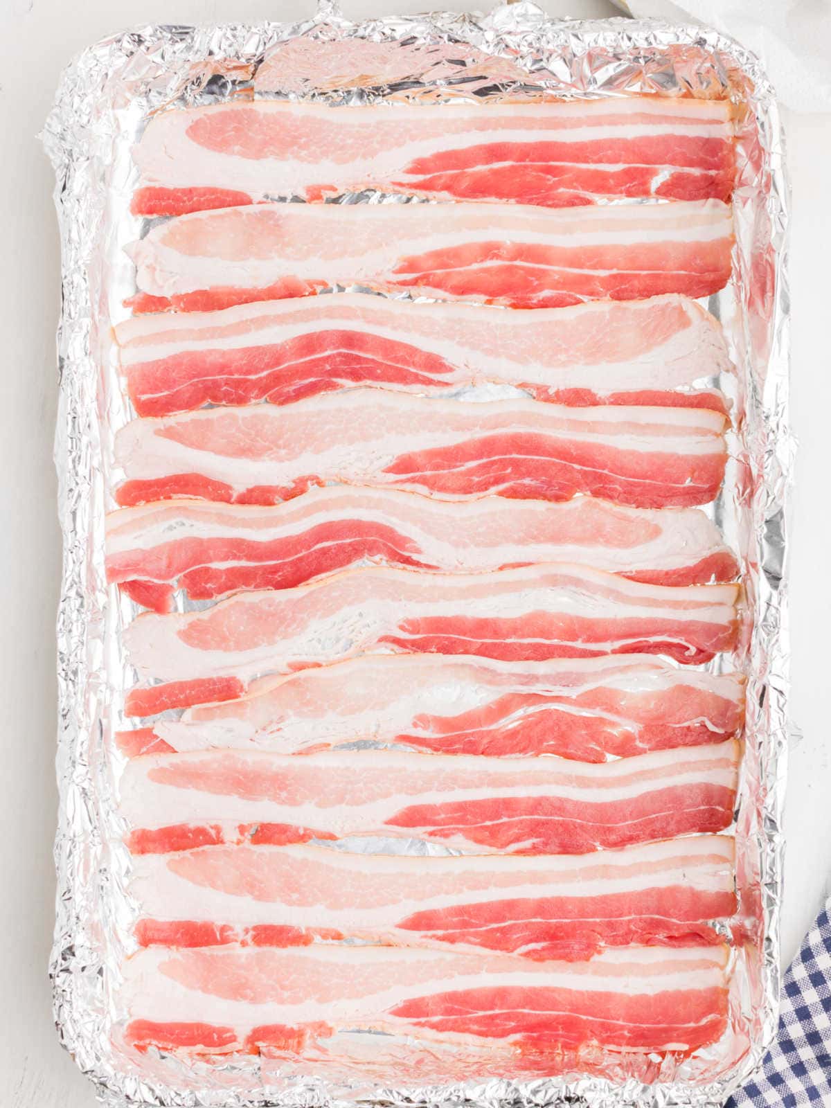 Uncooked bacon strips laid out in a single layer on a foil-lined baking sheet.
