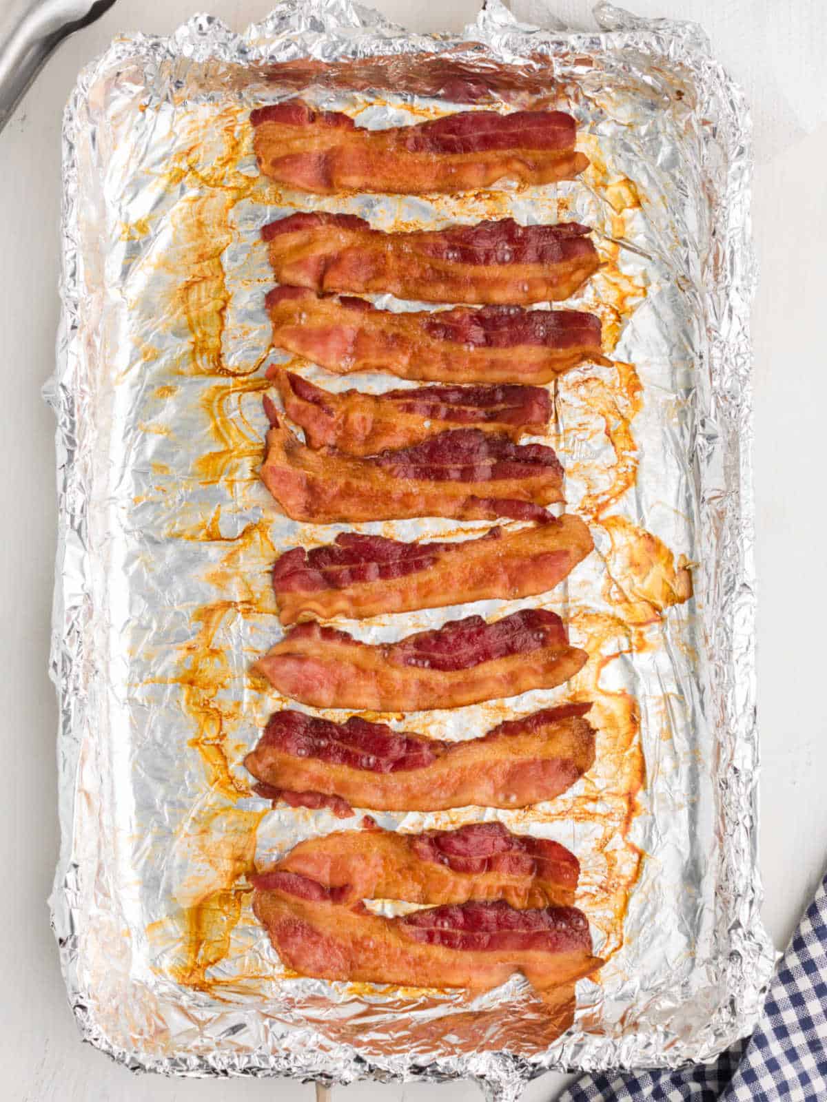 Cooked bacon strips arranged on a foil-lined baking sheet with some grease visible around the strips.