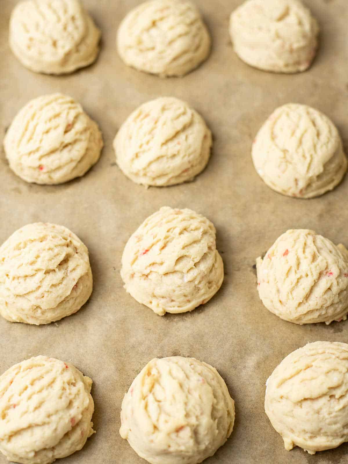 Scoops of unbaked cookie dough arranged in rows on a parchment-lined baking sheet.