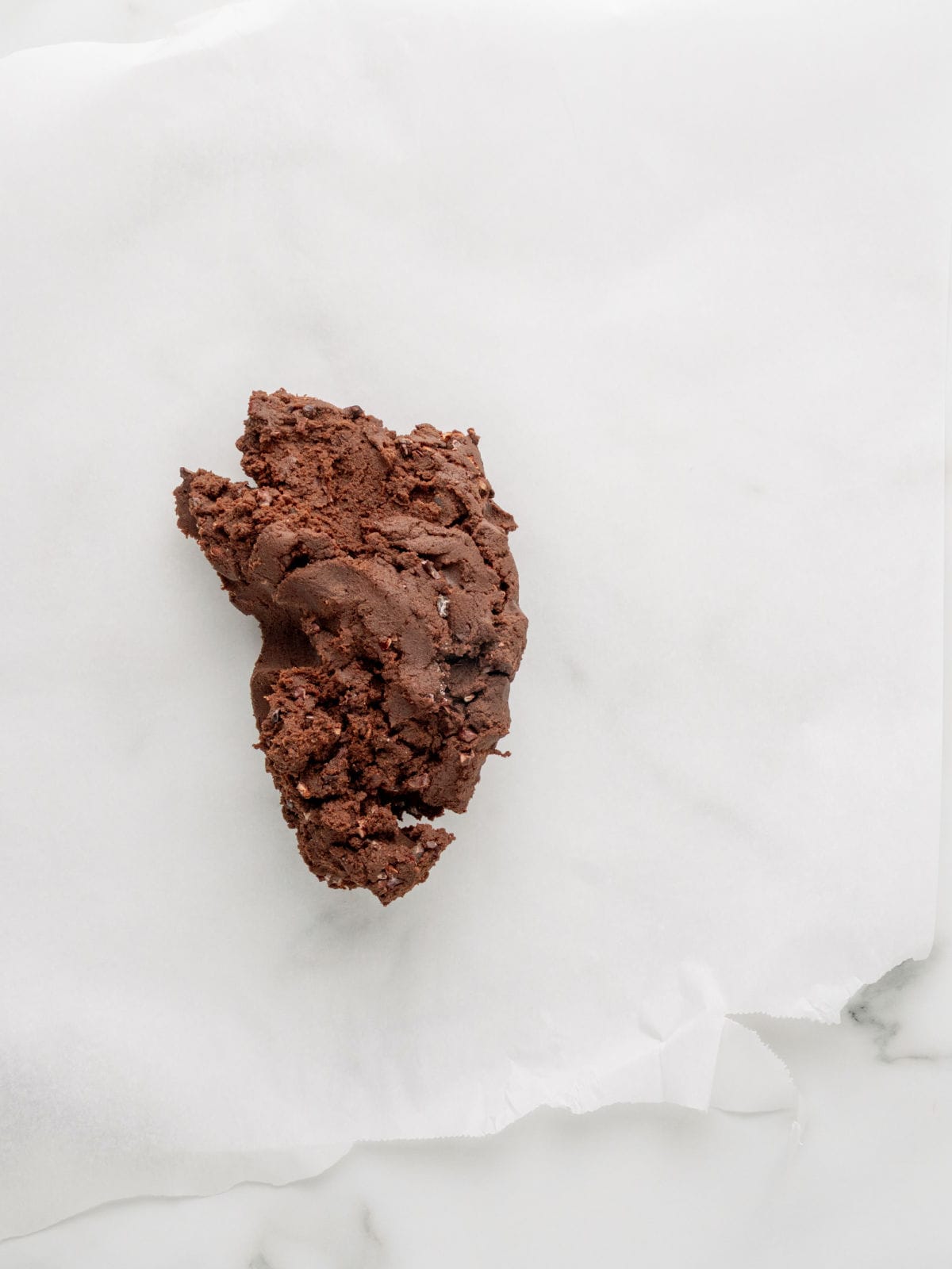 A mound of chocolate cookie dough sits on a sheet of parchment paper.