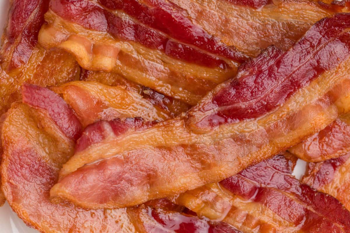Close-up image of several cooked bacon strips overlapping each other, showing crispy, reddish-brown texture and shiny surface.