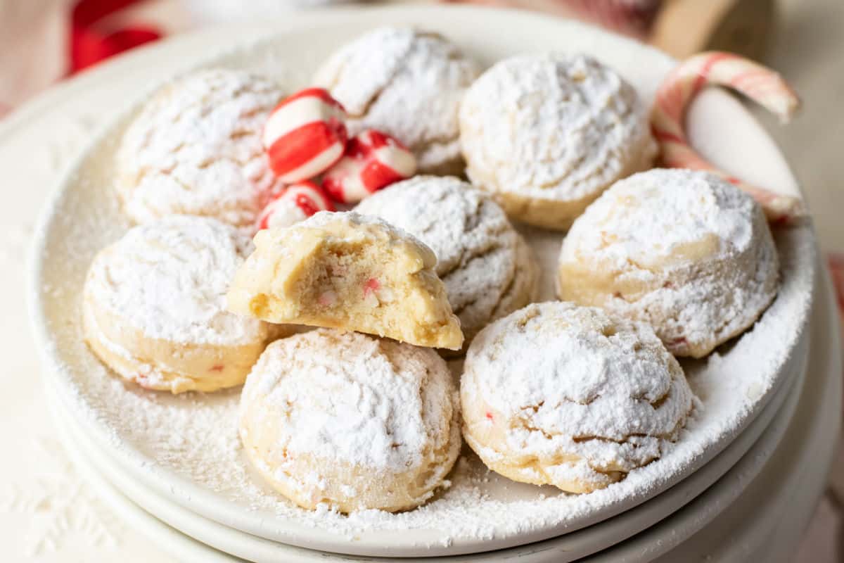 A plate of round cookies dusted with powdered sugar, with one cookie broken in half to show the inside, and peppermint candies in the background.