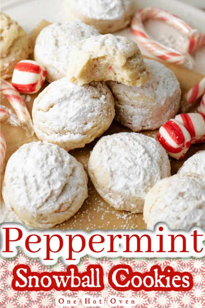 A plate of powdered sugar-coated peppermint snowball cookies with candy canes and peppermint candies, shown on parchment paper.