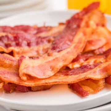 A close-up of several strips of oven baked cooked bacon on a white plate.
