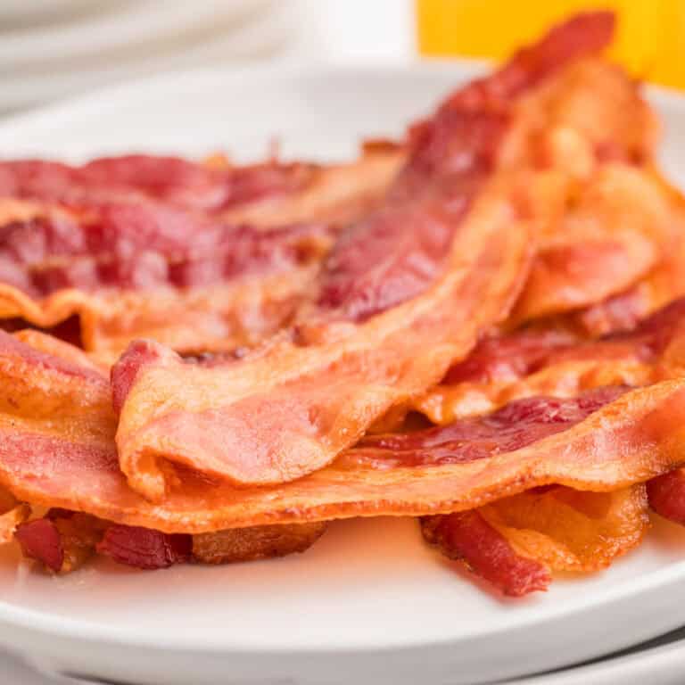 A close-up of several strips of oven baked cooked bacon on a white plate.