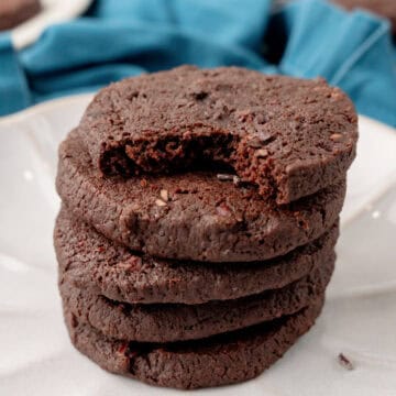 A stack of four chocolate shortbread cookies on a plate, with the top cookie showing a large bite taken out of it.