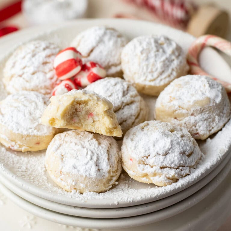 A plate of round cookies dusted with powdered sugar, with one cookie broken in half to show the inside, and some red and white candies in the background.