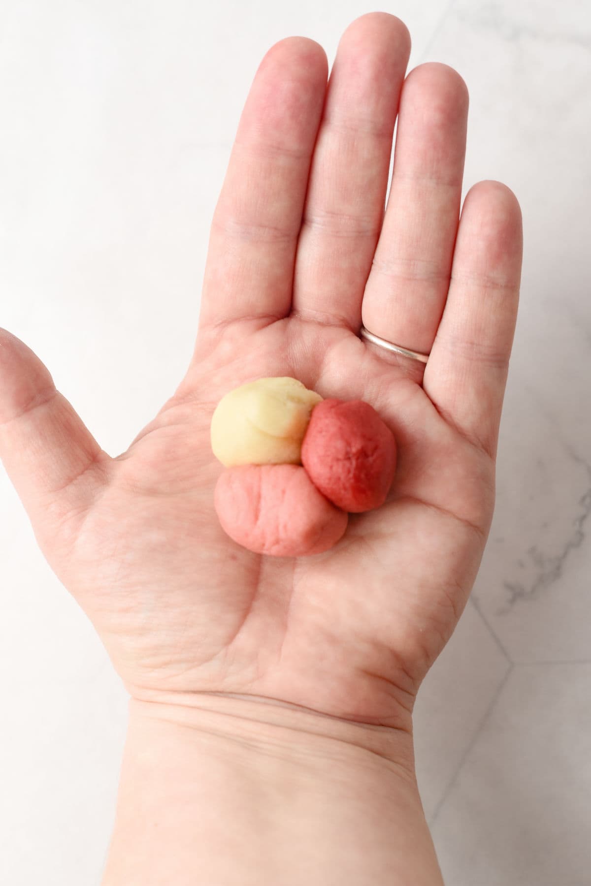 An open hand holds three small balls of dough in red and beige colors against a light background.