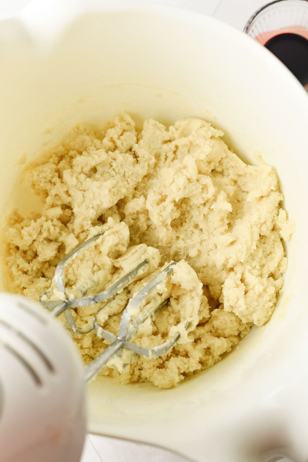 A mixing bowl containing sugar cookie dough being mixed with an electric hand mixer.