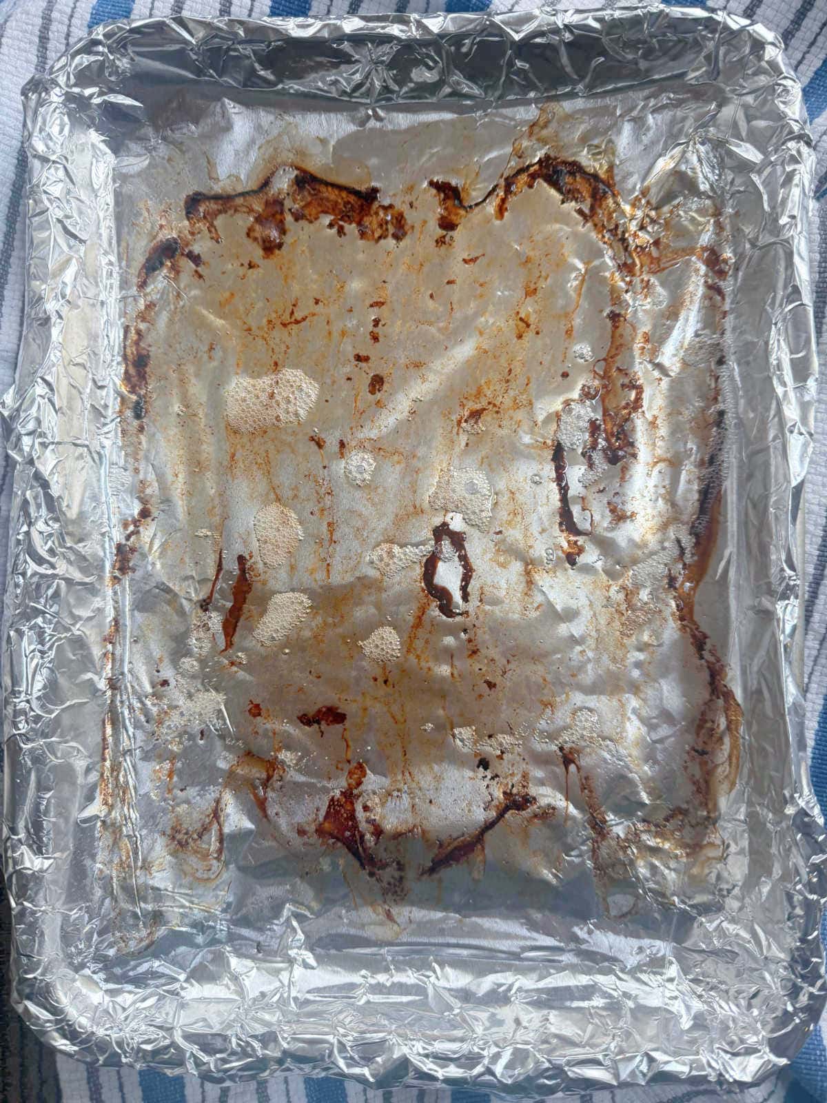A used baking tray lined with crumpled aluminum foil, showing bacon grease in pan.