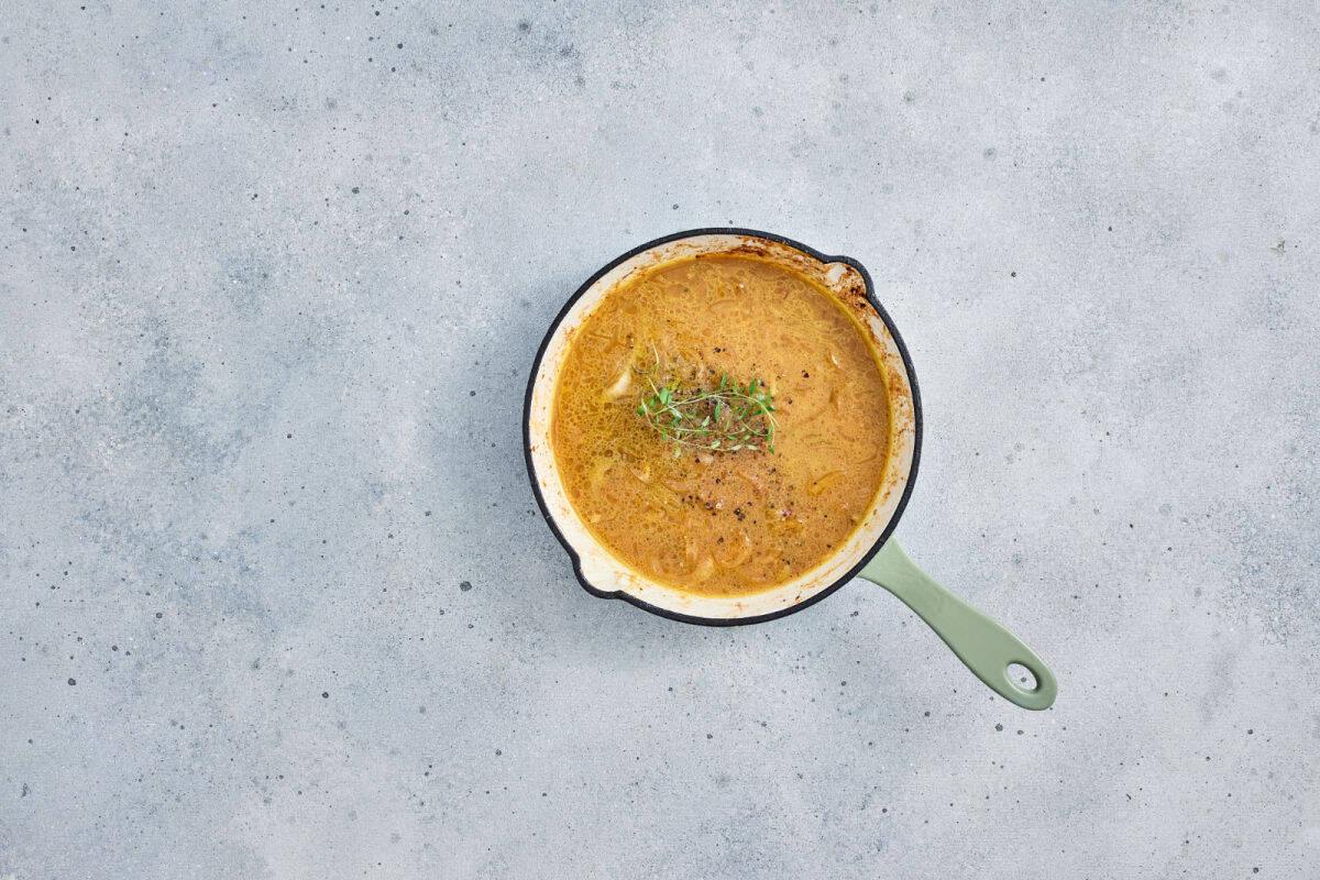 A round pan with a light green handle contains a bangers and mash onion gravy.