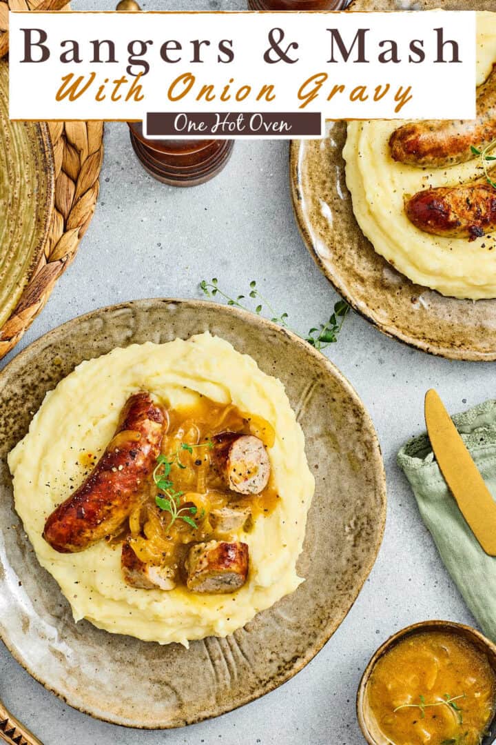 Plate of mashed potatoes topped with grilled sausages and onion gravy, garnished with herbs, with a knife, fork, and small bowl of gravy beside the plate.