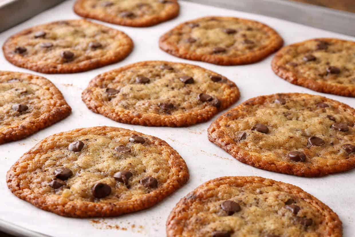 A tray of freshly baked chocolate chip cookies on parchment paper, arranged in rows and slightly golden brown around the edges.