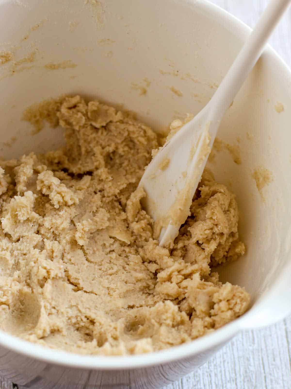 A mixing bowl containing cookie dough, with a white spatula partially buried in the mixture.