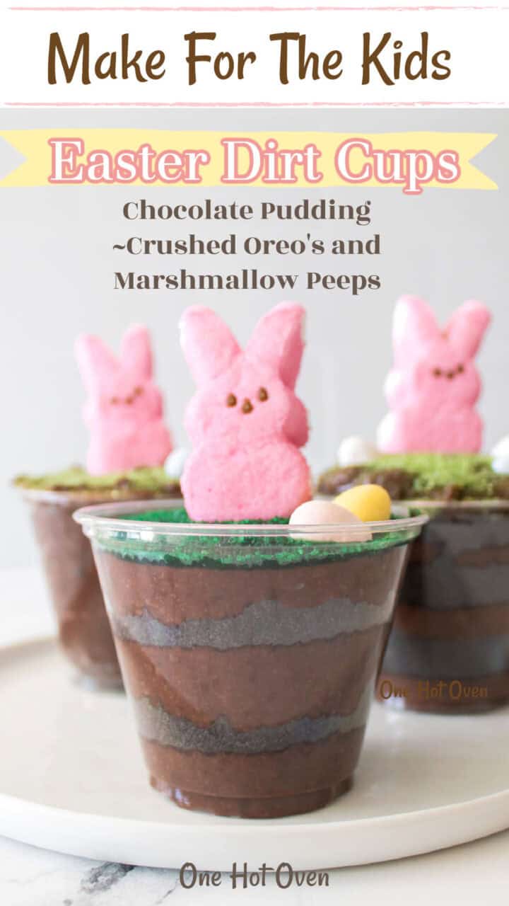 A clear plastic cup filled with chocolate pudding, crushed Oreos, and topped with a pink marshmallow bunny and candy eggs; two similar cups are in the background.