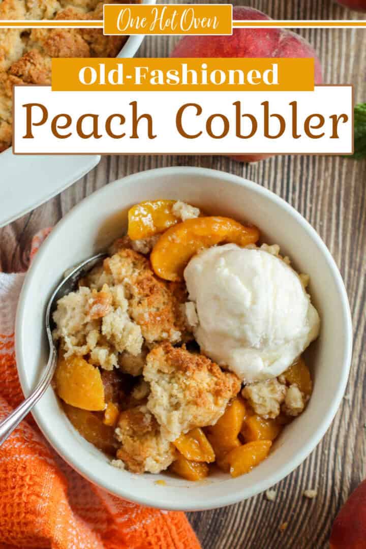 A bowl of peach cobbler topped with a scoop of vanilla ice cream sits on a wooden table, with a spoon and peaches nearby.