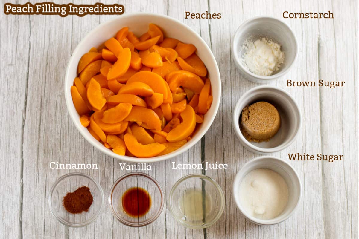 A bowl of sliced peaches with small bowls of cornstarch, brown sugar, white sugar, lemon juice, vanilla, and cinnamon on a wooden surface, labeled as peach filling ingredients.