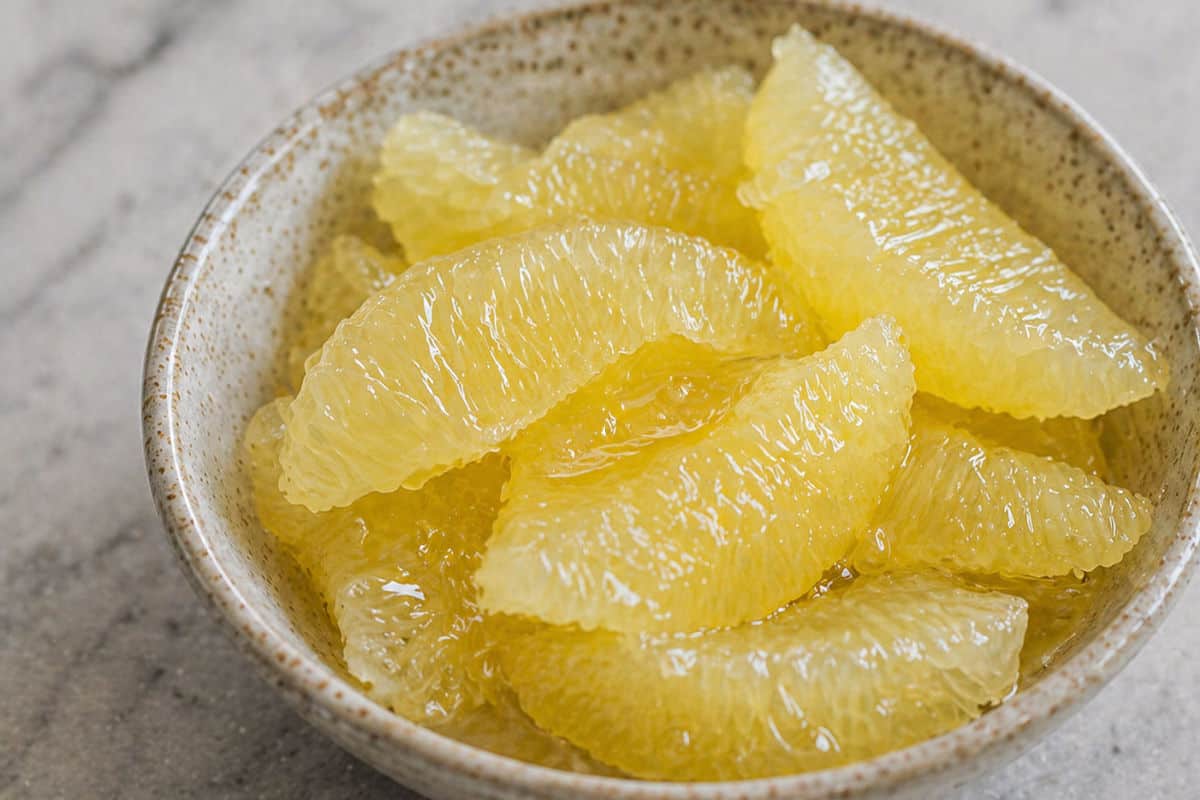 A ceramic bowl filled with supremed yellow lemon pieces on a light-colored surface.