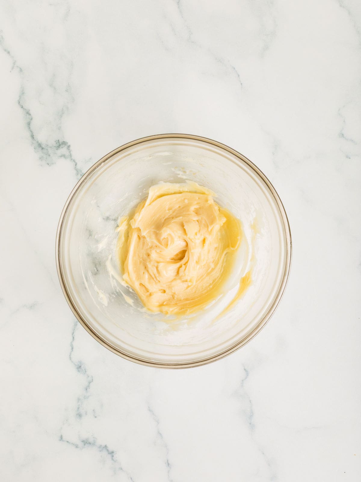 A glass bowl containing creamed butter and sugar on a white marble surface.