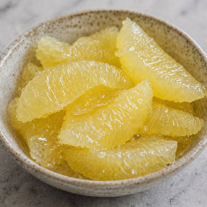 A bowl filled with peeled and segmented pomelo fruit on a light-colored surface.