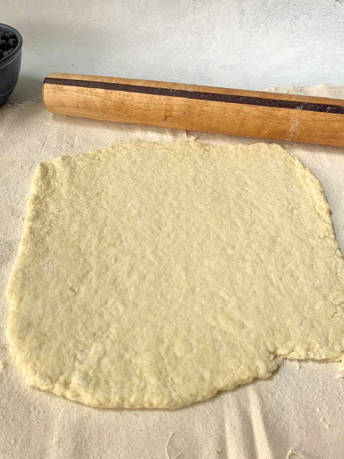 A sheet of scone dough rolled out on a floured surface with a wooden rolling pin placed above it.