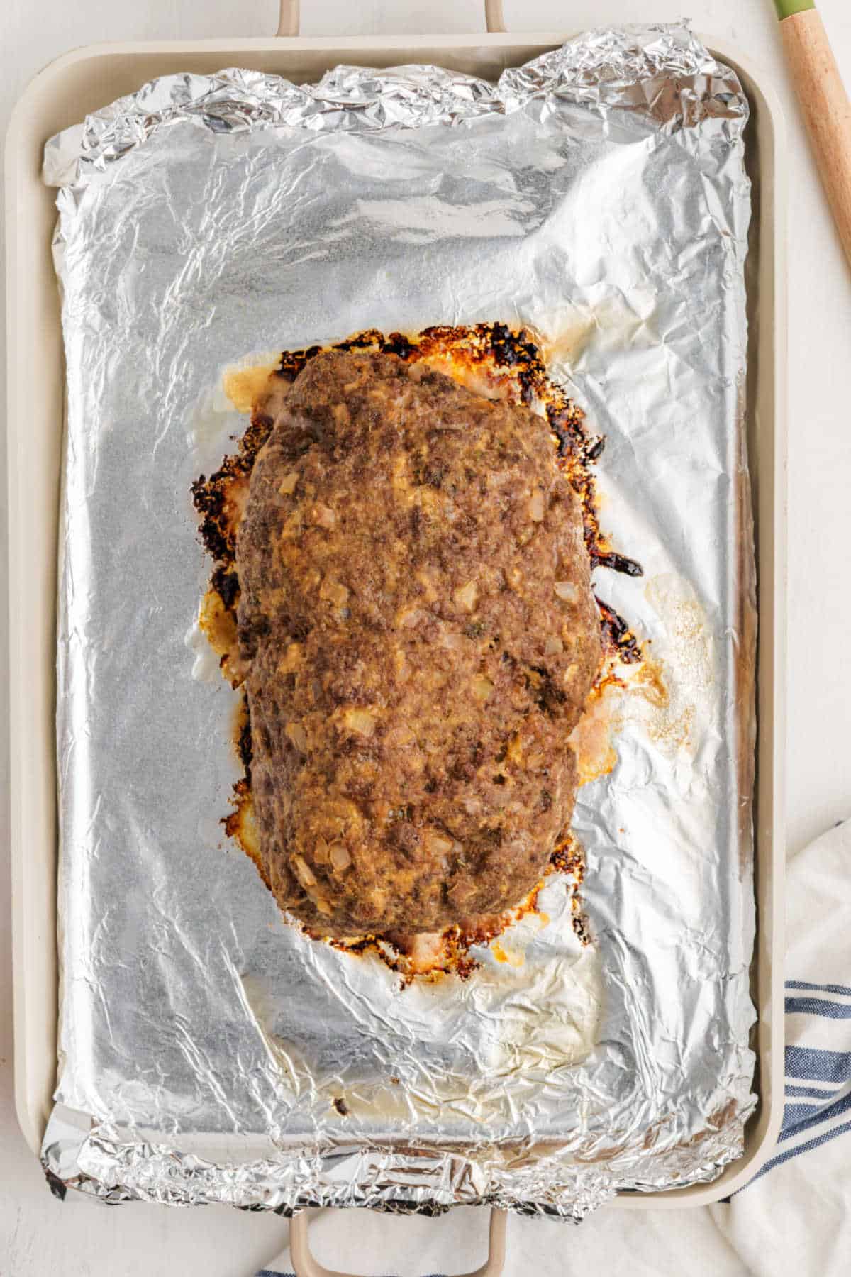 A baked meatloaf sits on a foil-lined baking sheet.