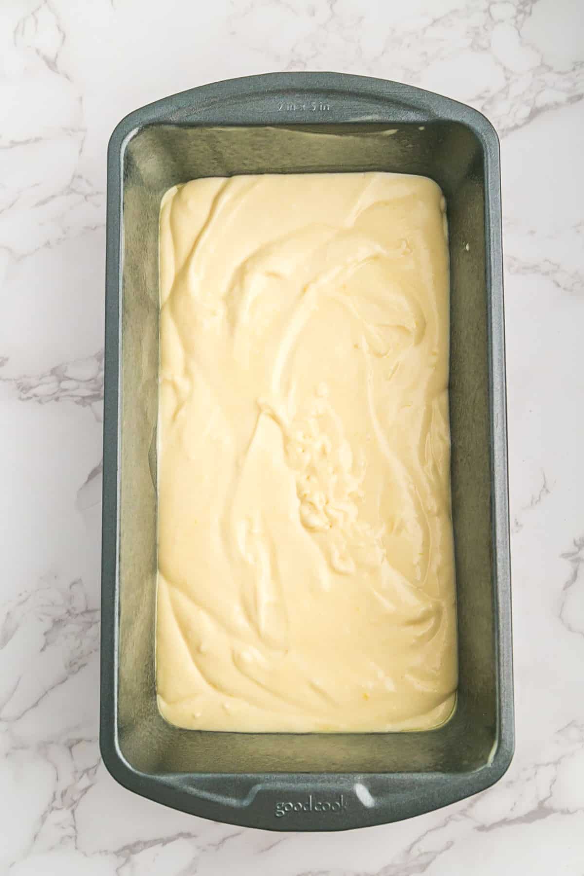 A metal loaf pan filled with uncooked lemon loaf cake batter sits on a marble countertop.