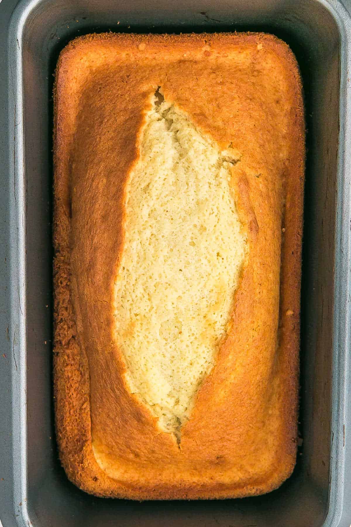 A golden-brown lemon loaf cake with a split top, baked in a rectangular metal pan.