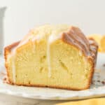 A sliced loaf of pound cake with white icing drizzled on top, displayed on a white plate.