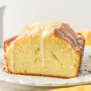 A sliced loaf of pound cake with white icing drizzled on top, displayed on a white plate.
