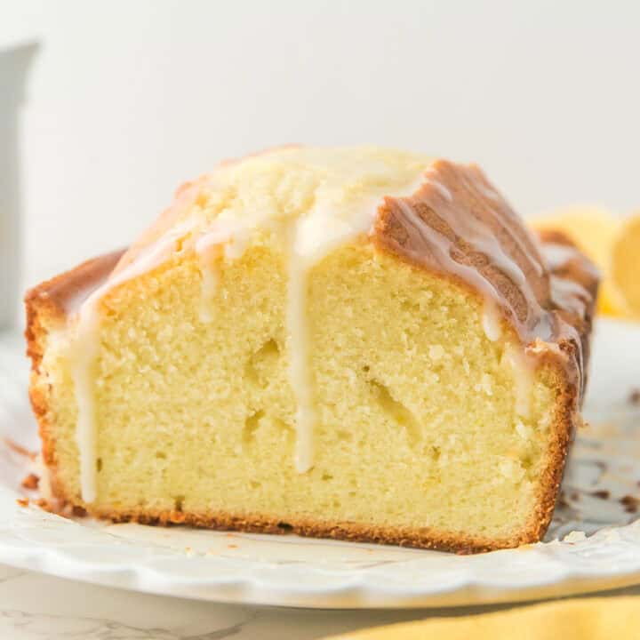 A sliced loaf of pound cake with white icing drizzled on top, displayed on a white plate.
