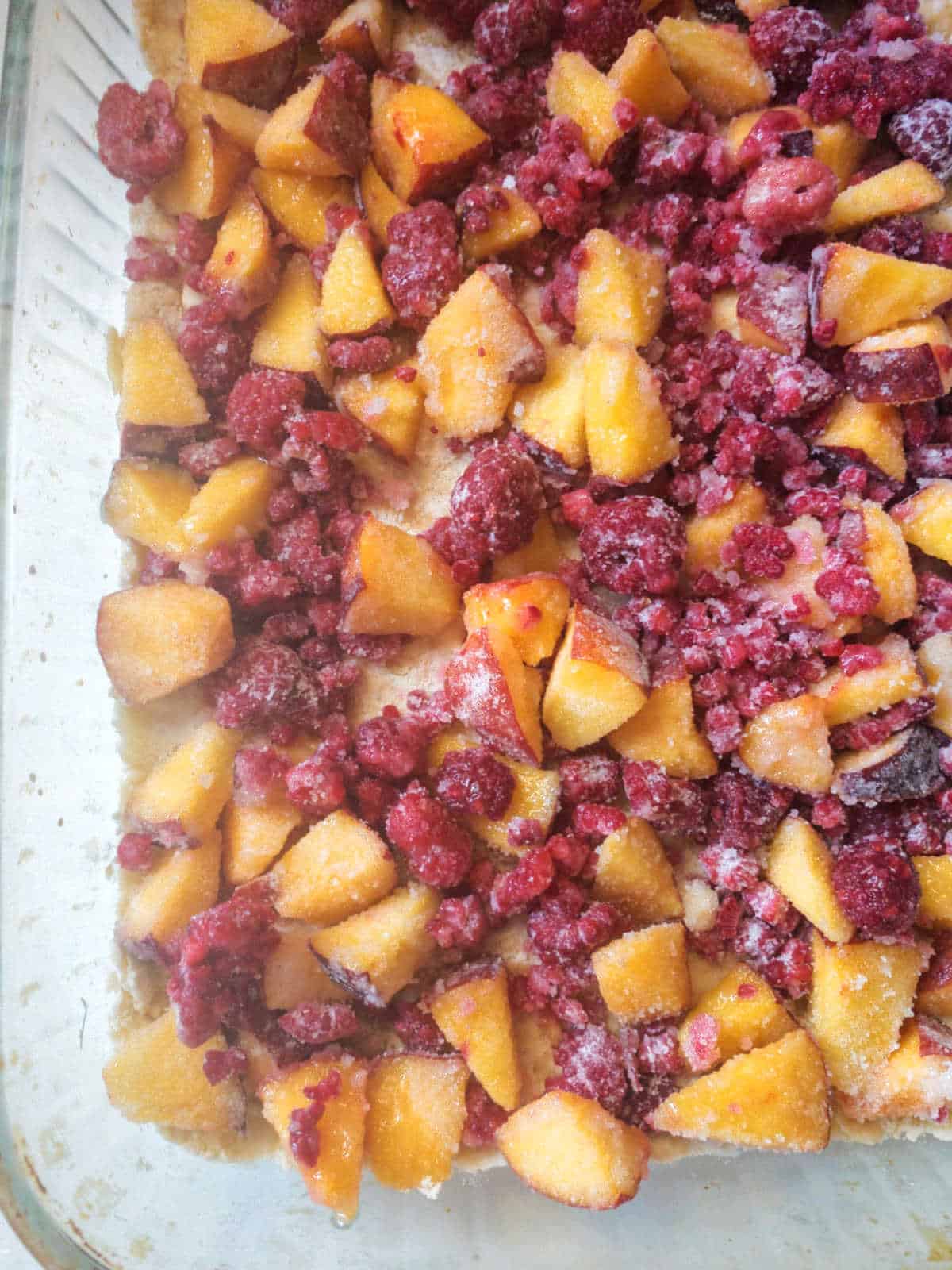 A baking dish filled with a mixture of chopped peaches and raspberries, sprinkled with sugar, ready to be baked.