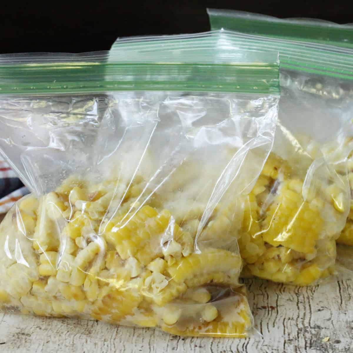 Several clear resealable plastic bags filled with cut corn kernels are placed on a light wooden surface.