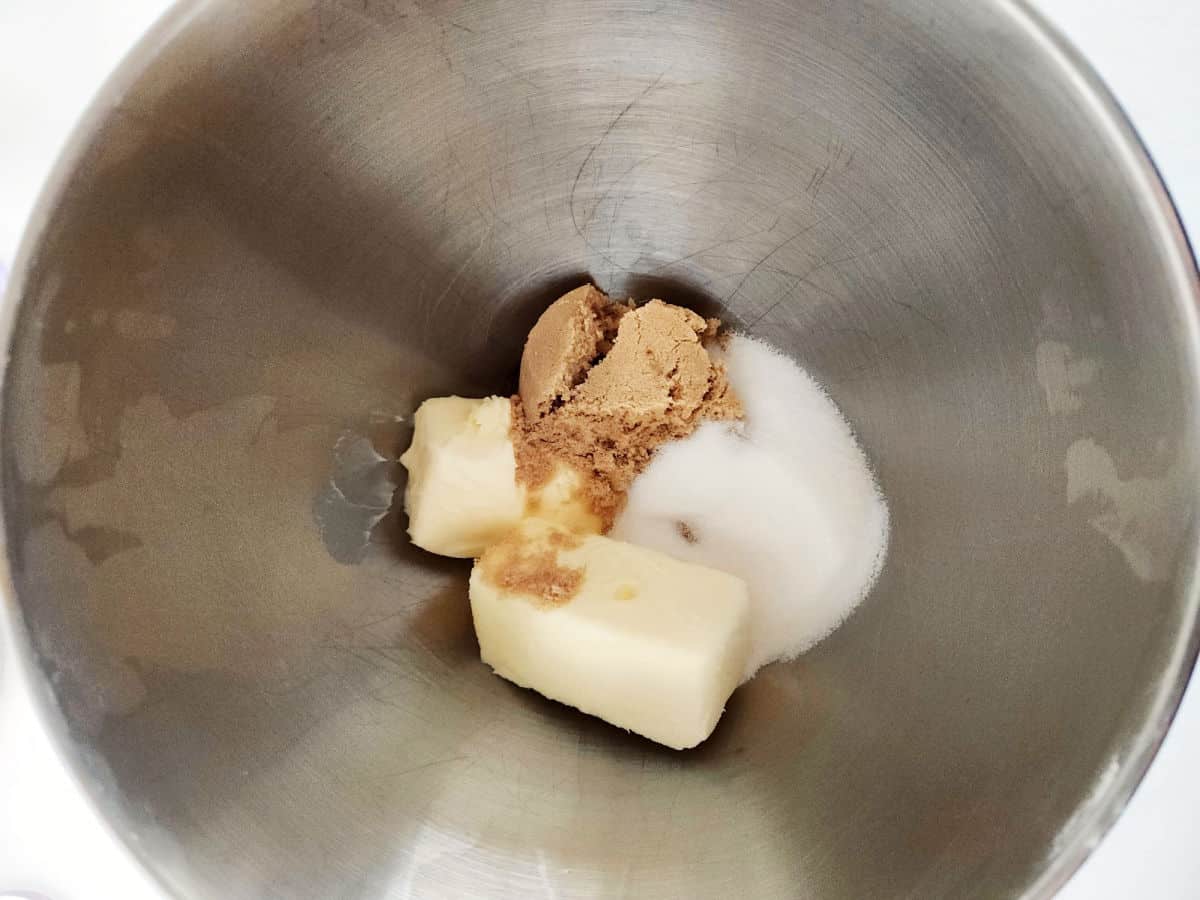 A metal mixing bowl containing butter, brown sugar, and white sugar.