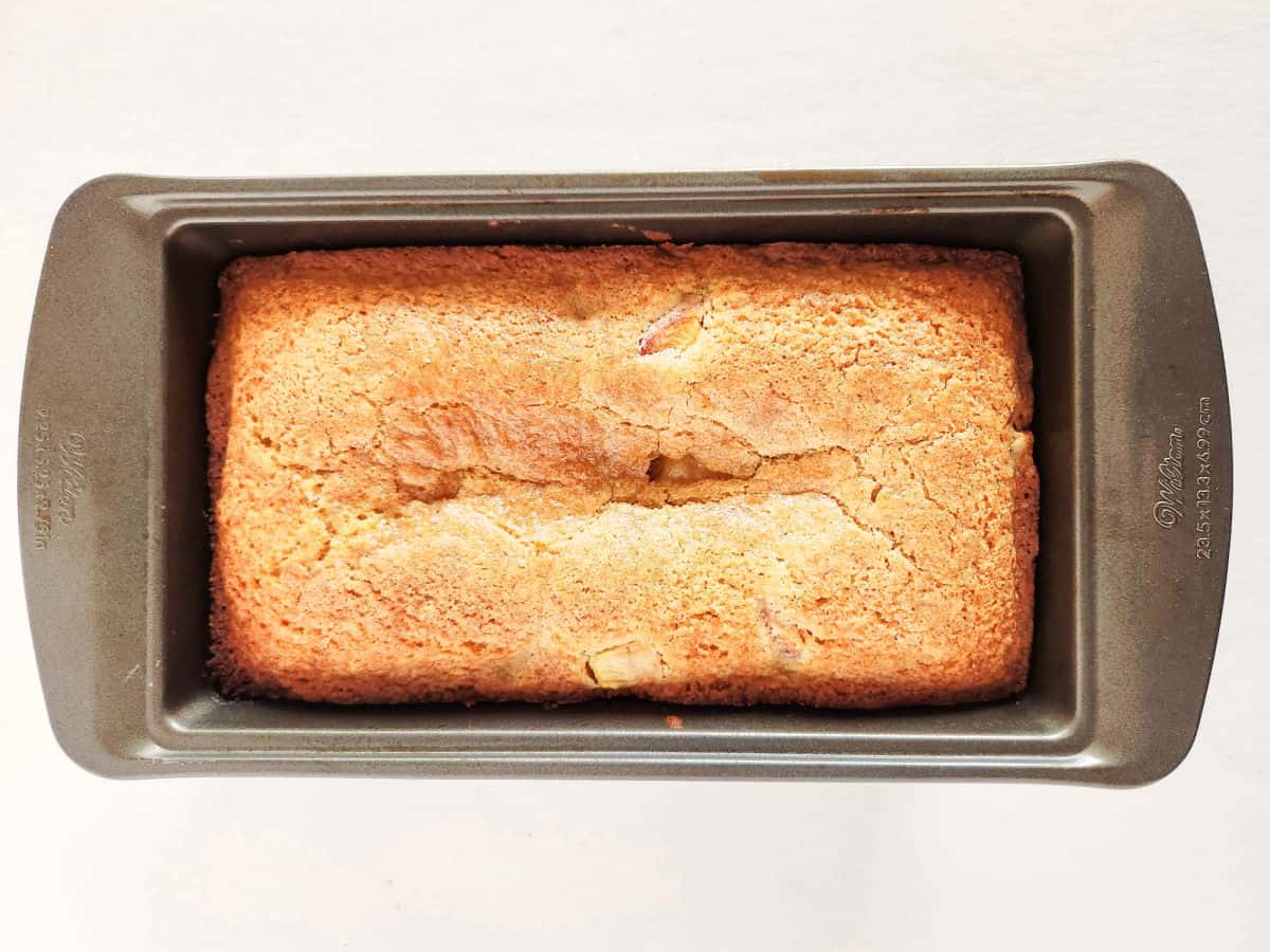 A golden-brown loaf of bread in a rectangular metal baking pan, viewed from above on a white background.