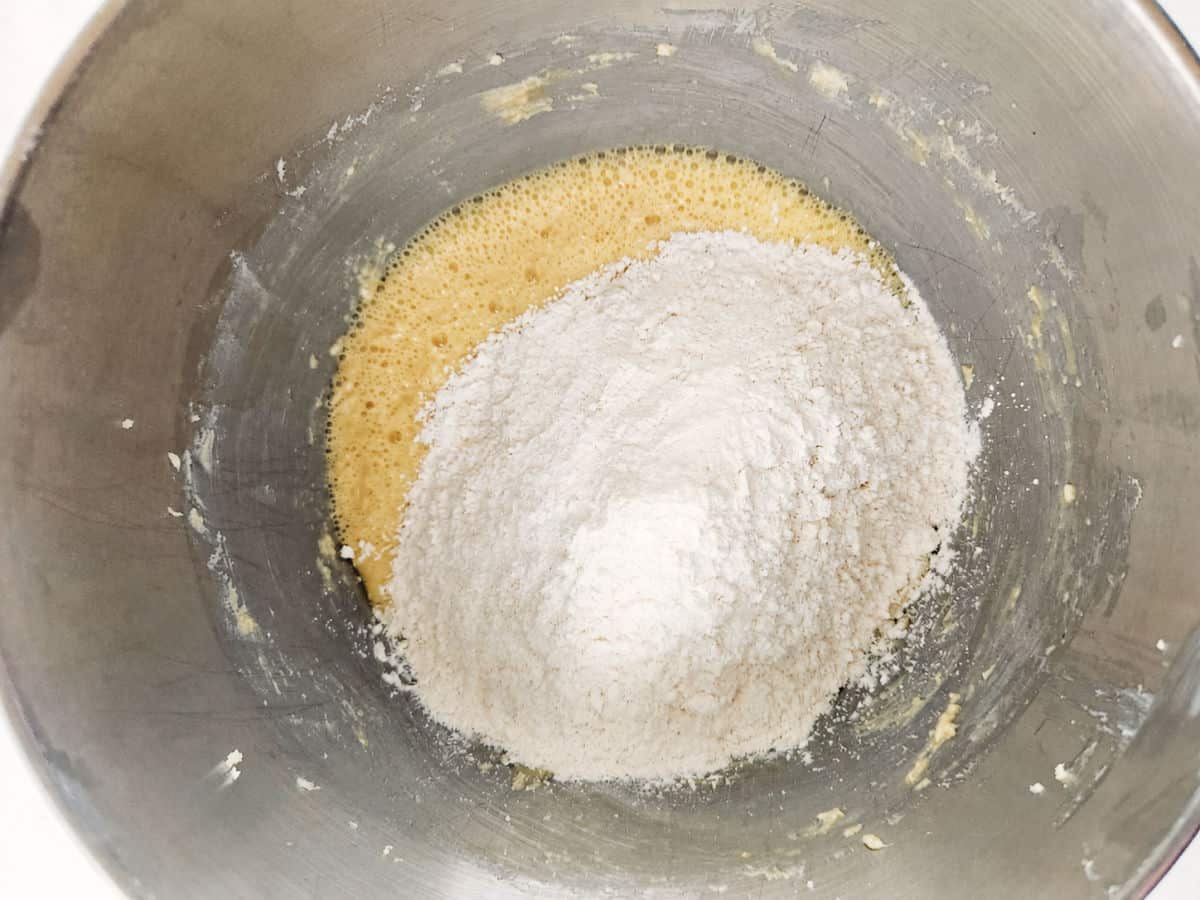 A metal mixing bowl containing whisked wet ingredients with flour piled on top, ready to be mixed together.