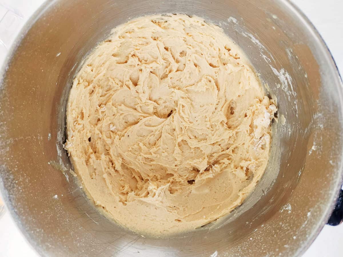 A large stainless steel mixing bowl filled with creamy, light brown cookie dough, viewed from above.
