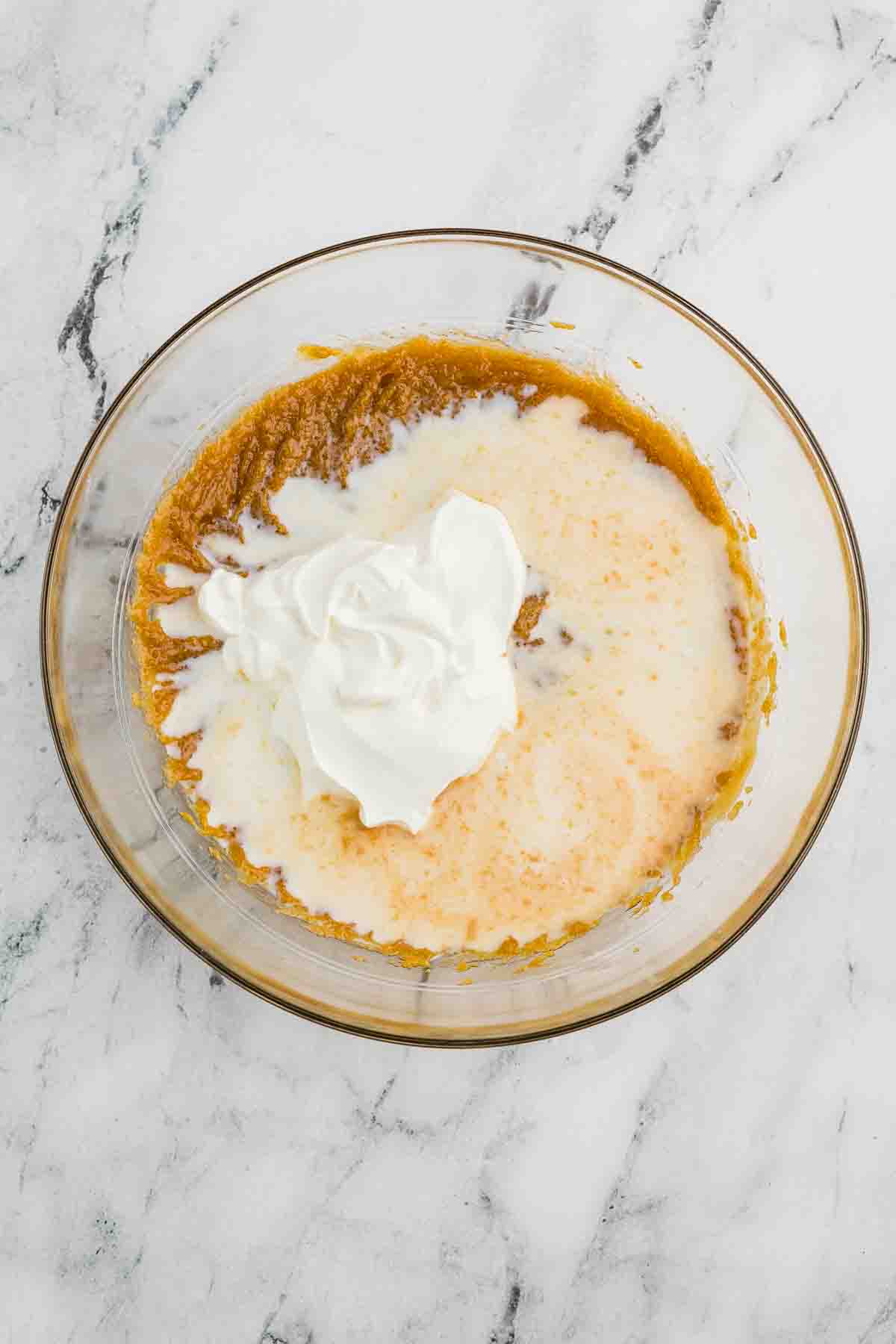 A glass bowl with a mixture of pumpkin puree, cream, and whipped topping on a white marble surface.
