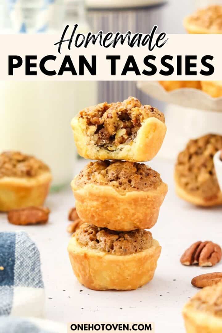 A stack of three pecan tassies on a table, with one tassie on top bitten to show the pecan filling. Other tassies and pecans are scattered around. Text reads "Homemade Pecan Tassies.