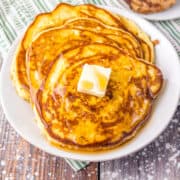 A stack of pancakes topped with a pat of butter and drizzled with syrup, served on a white plate.